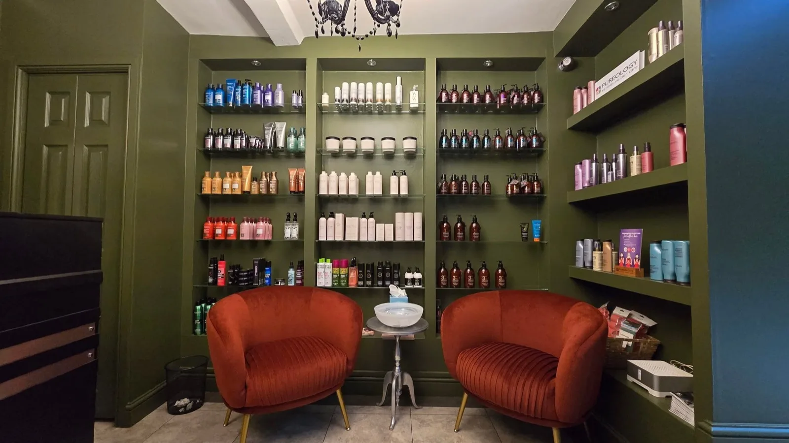 Salon fit-out after: alcove and walls painted deep olive green, fitted with glass retail shelving