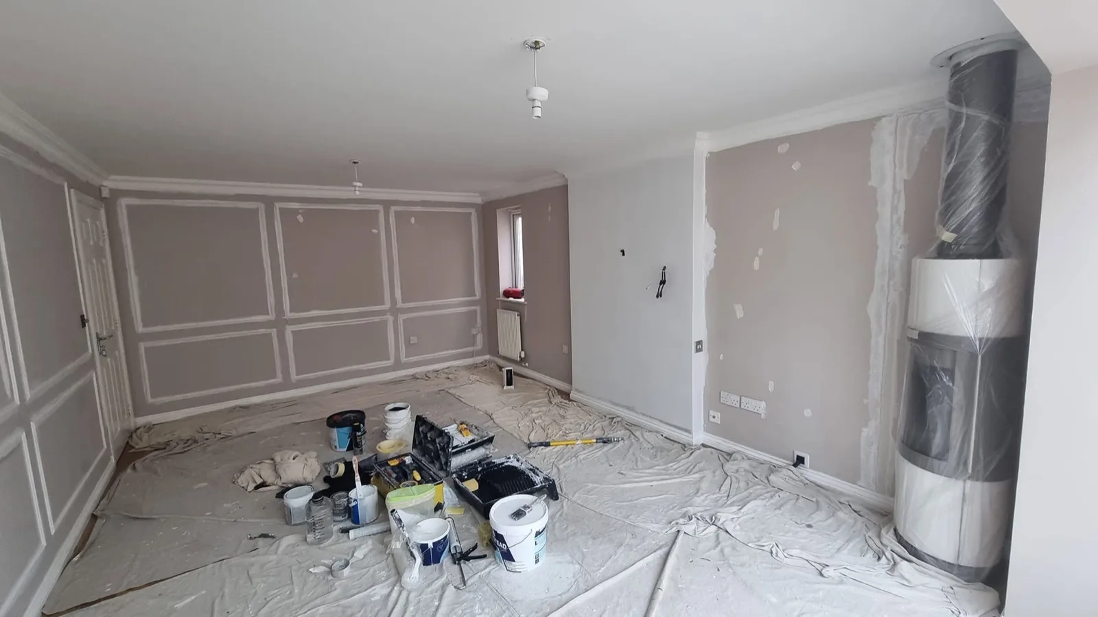 Living room before: bare plastered walls, fitted panelling and dust sheets mid-prep
